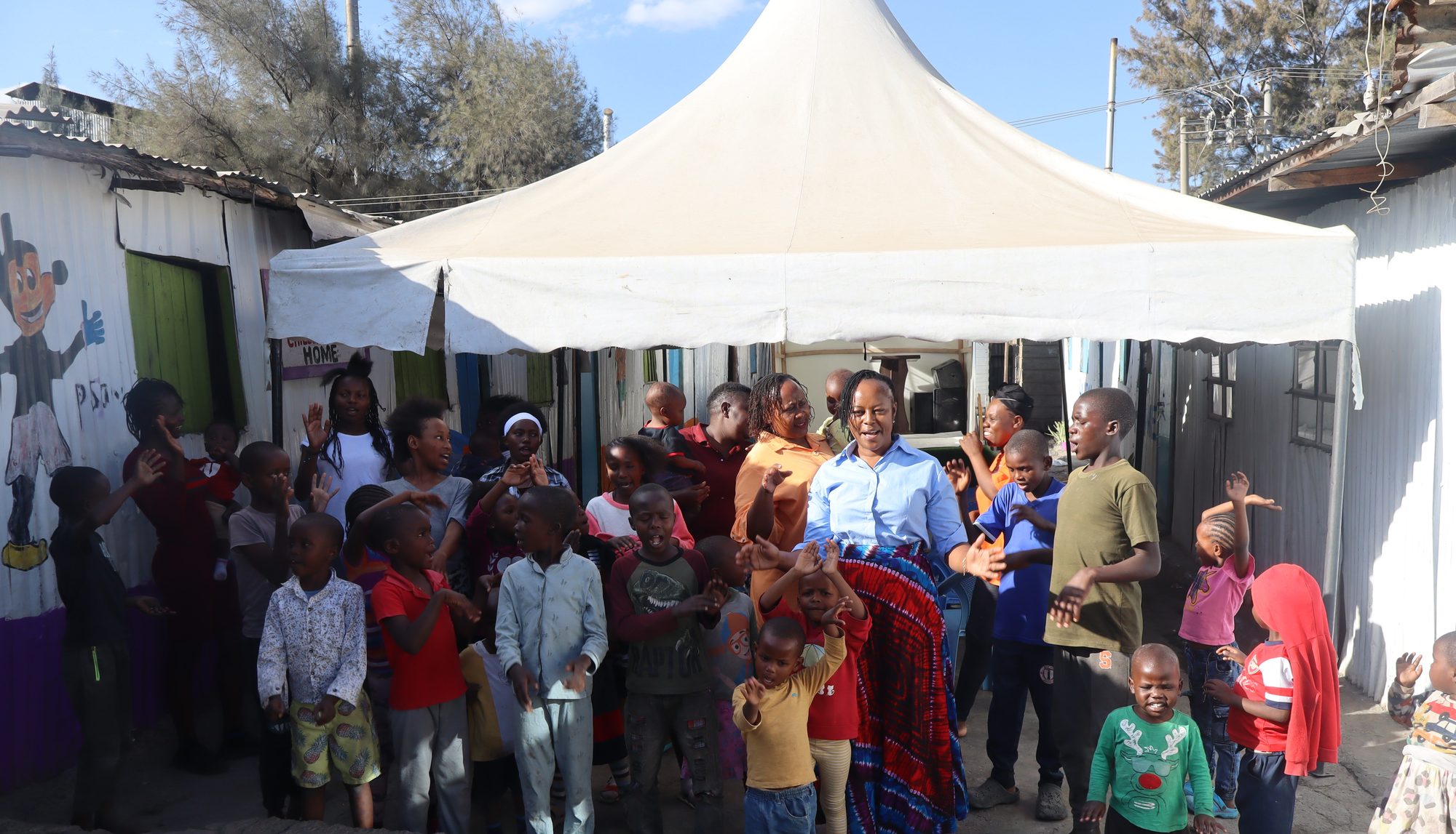 Children and caregivers under the tent at Nuru Toto